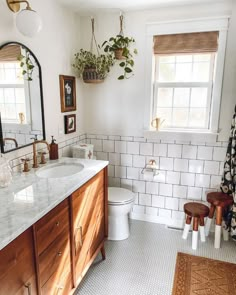 a bathroom with white tile and wooden cabinetry is pictured in this image, there are potted plants on the window sill