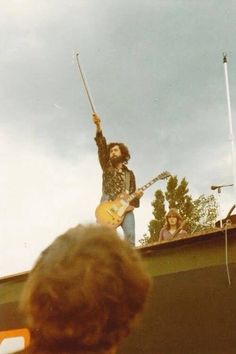 an old photo of a man playing guitar on top of a roof with other people watching