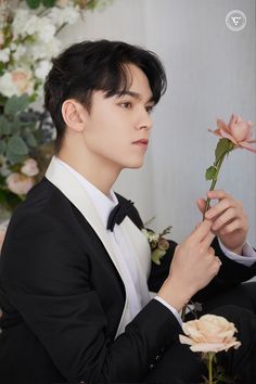 a young man in a tuxedo holding a rose and looking at the camera