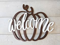 a wooden sign that says welcome with a pumpkin in the center on a white wood background