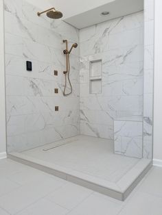 a walk in shower sitting next to a white tiled wall and floor with gold faucet