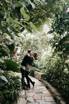 a man and woman kissing in the middle of a garden with lots of greenery