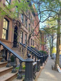 a row of brownstone townhouses on a city street with trees and flowers in the foreground