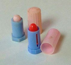 two blue and one pink lipstick tubes on a white surface with an orange ball in the middle