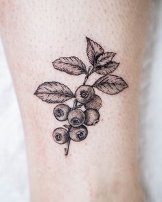 a small tattoo on the leg of a woman with berries and leaves growing out of it