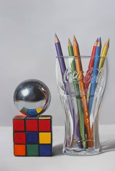 a glass vase filled with colored pencils next to a rubik cube and ball