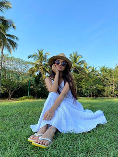 a woman sitting in the grass wearing a hat and sunglasses