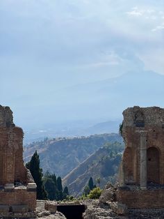 the ruins of an ancient roman city with mountains in the background and trees on either side