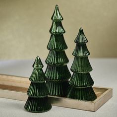 three green glass christmas trees sitting on top of a wooden tray next to a mirror