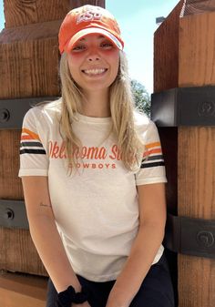 a young woman sitting on top of a wooden bench wearing a hat and holding her hands in her pockets