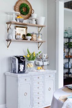 a kitchen with white cabinets and shelves filled with dishes on top of each shelf, next to a coffee maker