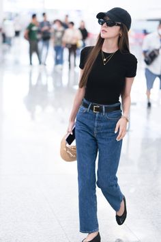 a woman in black shirt and jeans walking through an airport with her hand on her hip