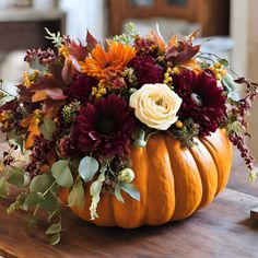 a pumpkin filled with flowers on top of a wooden table