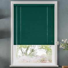 a window with green blinds in front of it and flowers on the table next to it