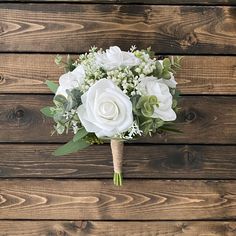 a bridal bouquet with white flowers and greenery on a wooden background, ready to be used as a bride's bouquet