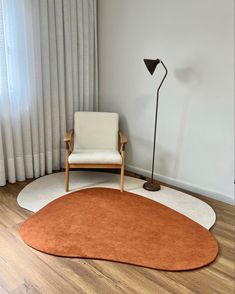 an orange and white rug with a chair in the corner next to a lamp on a wooden floor