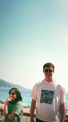 two people standing next to each other near the ocean