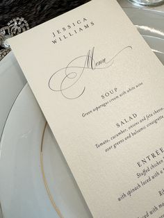 a white plate topped with a menu next to a silver and black table cloth covered place setting