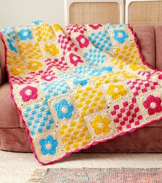 a crocheted blanket is sitting on a couch in front of a pink chair