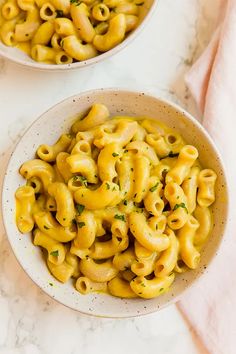 two bowls filled with macaroni and cheese on top of a marble countertop