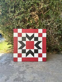 a red and black checkered square with an arrow on the center is sitting in front of some bushes