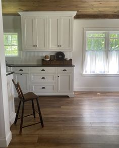 an empty kitchen with white cabinets and wood flooring, along with a wooden bar stool