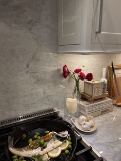 fish and vegetables cooking in a skillet on the stove top with flowers next to it