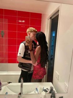 two people standing in front of a bathroom mirror with red tiles on the wall behind them