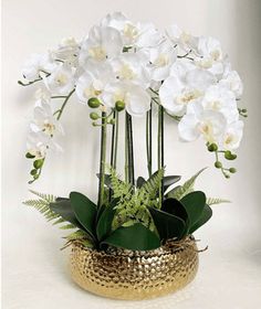 white flowers are in a gold vase with greenery