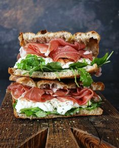 a sandwich with meat, lettuce and cheese on it sitting on top of a wooden cutting board