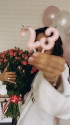 a woman holding flowers and balloons in front of her face with the number 28 on it