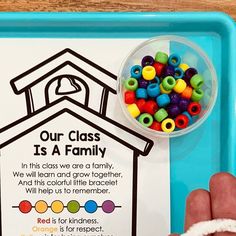 a child's hand next to a blue tray with beads and a sign that says our class is a family