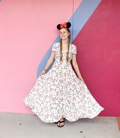 a woman in a white dress standing next to a pink and blue wall wearing a minnie mouse ears headband