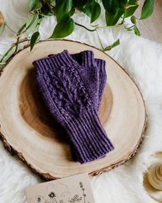 a pair of purple knitted mittens sitting on top of a wooden slice next to a plant