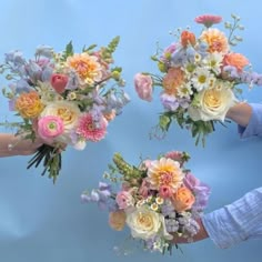 three bouquets of flowers are being held by two hands in front of a blue background