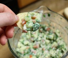 a hand holding a tortilla chip over a bowl of guacamole