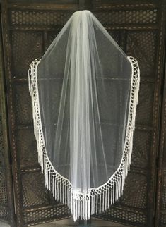 a white veil hanging from the side of a wooden door with fringes on it