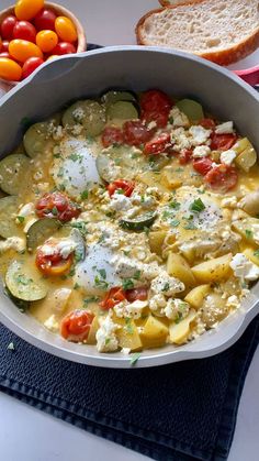 a pan filled with eggs and vegetables on top of a blue cloth next to bread