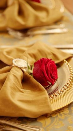 a red rose sitting on top of a plate with napkins and silverware next to it