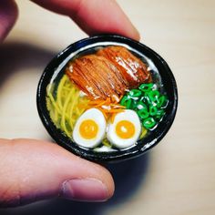 a hand holding a small bowl with noodles, eggs and bacon in it's center