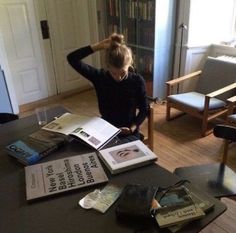 a woman sitting at a table with several books on top of it in front of a bookcase