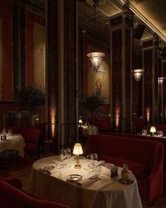 a dimly lit dining room with red chairs and white tablecloths, along with two lamps on either side of the tables