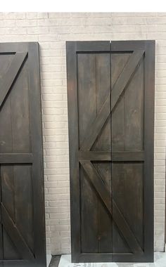 two large wooden doors sitting next to each other in front of a white brick wall