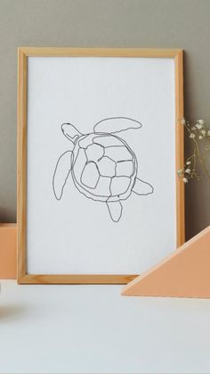 a drawing of a turtle in a wooden frame on a table next to some flowers