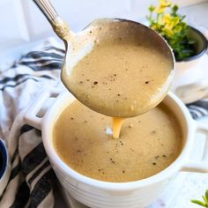 a spoon full of gravy being lifted from a white bowl with flowers in the background