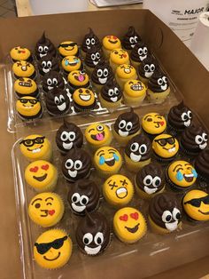 a box filled with lots of yellow cupcakes covered in chocolate frosted smiley faces