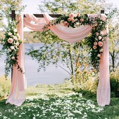 an outdoor wedding ceremony setup with pink drapes, flowers and greenery on the grass