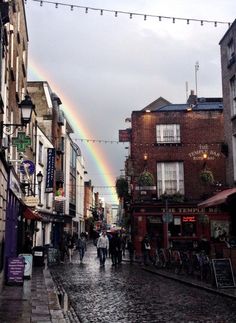 a rainbow shines in the sky over a cobblestone street lined with buildings