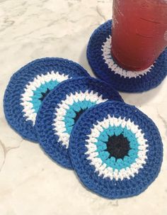 three crocheted coasters on a table with a red drink in the background