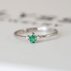 an emerald and diamond ring sitting on top of a white surface with other items in the background